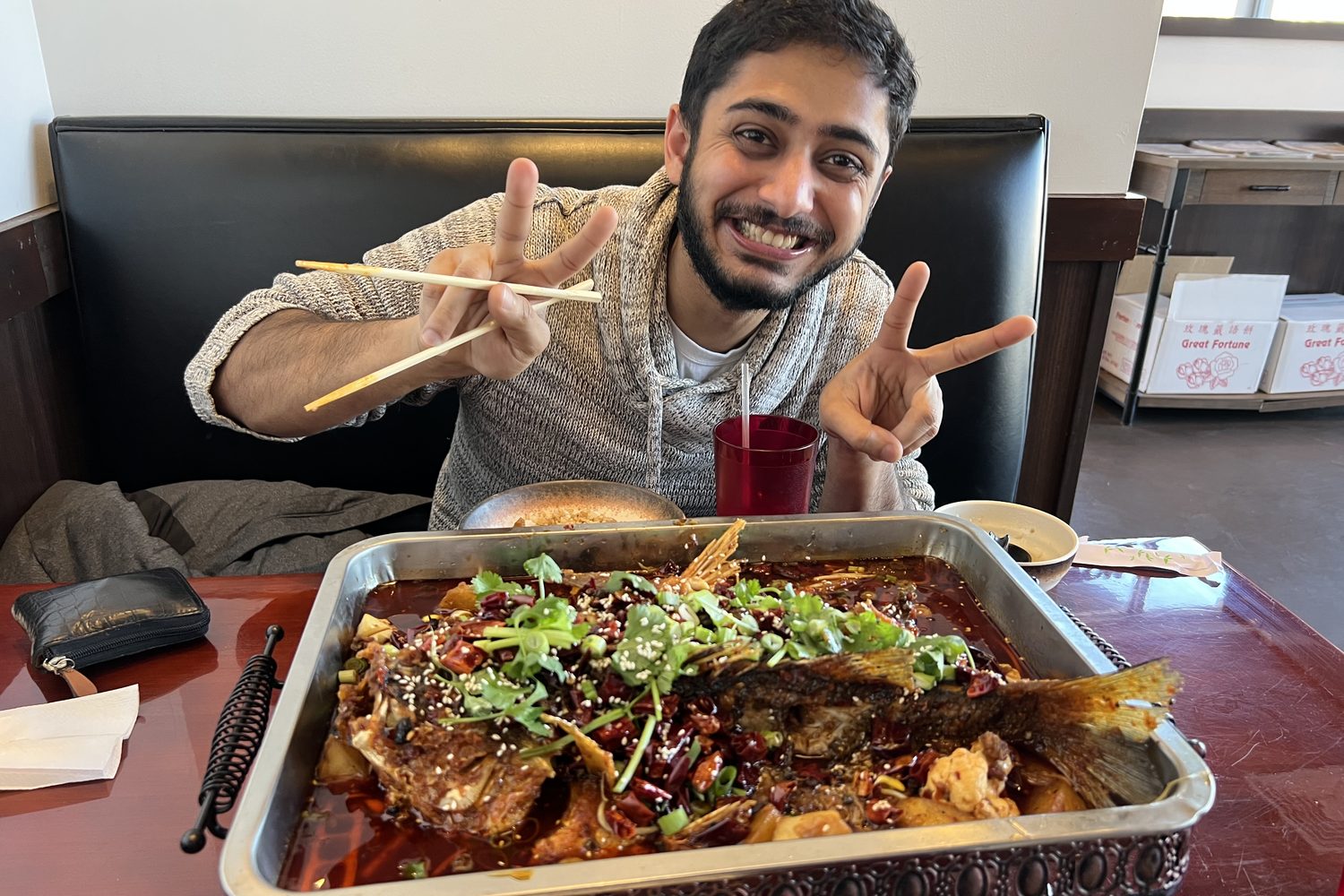 A friend grinning behind a whole fish in chilli oil, both hands up in peace signs.