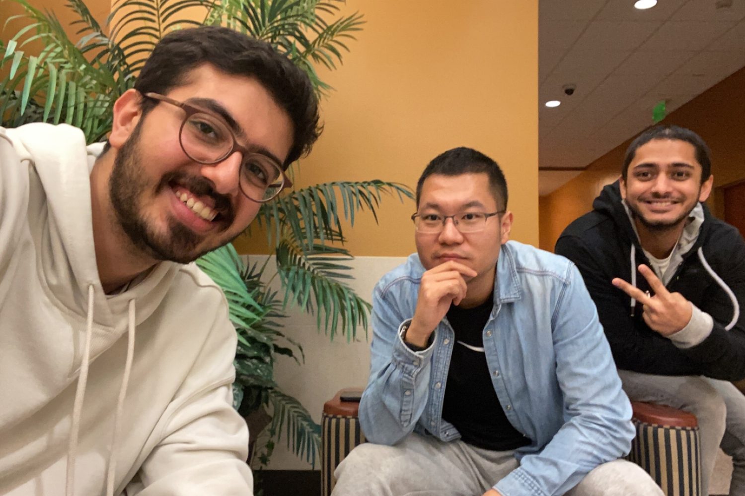 Three friends leaning into a selfie in a hotel corridor, two of them making peace signs.